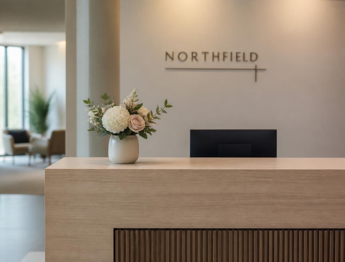 Essential arrangement — a compact 16-inch floral arrangement in a matte ceramic vase on the corner of a light oak reception desk in a neutral lobby — reference visual shown straight on at desk height.